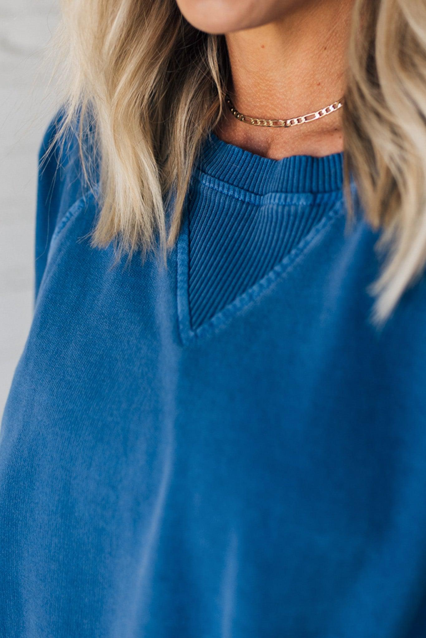A woman wearing a blue ribbed accent pocketed pullover with dolman sleeves and a round neckline.