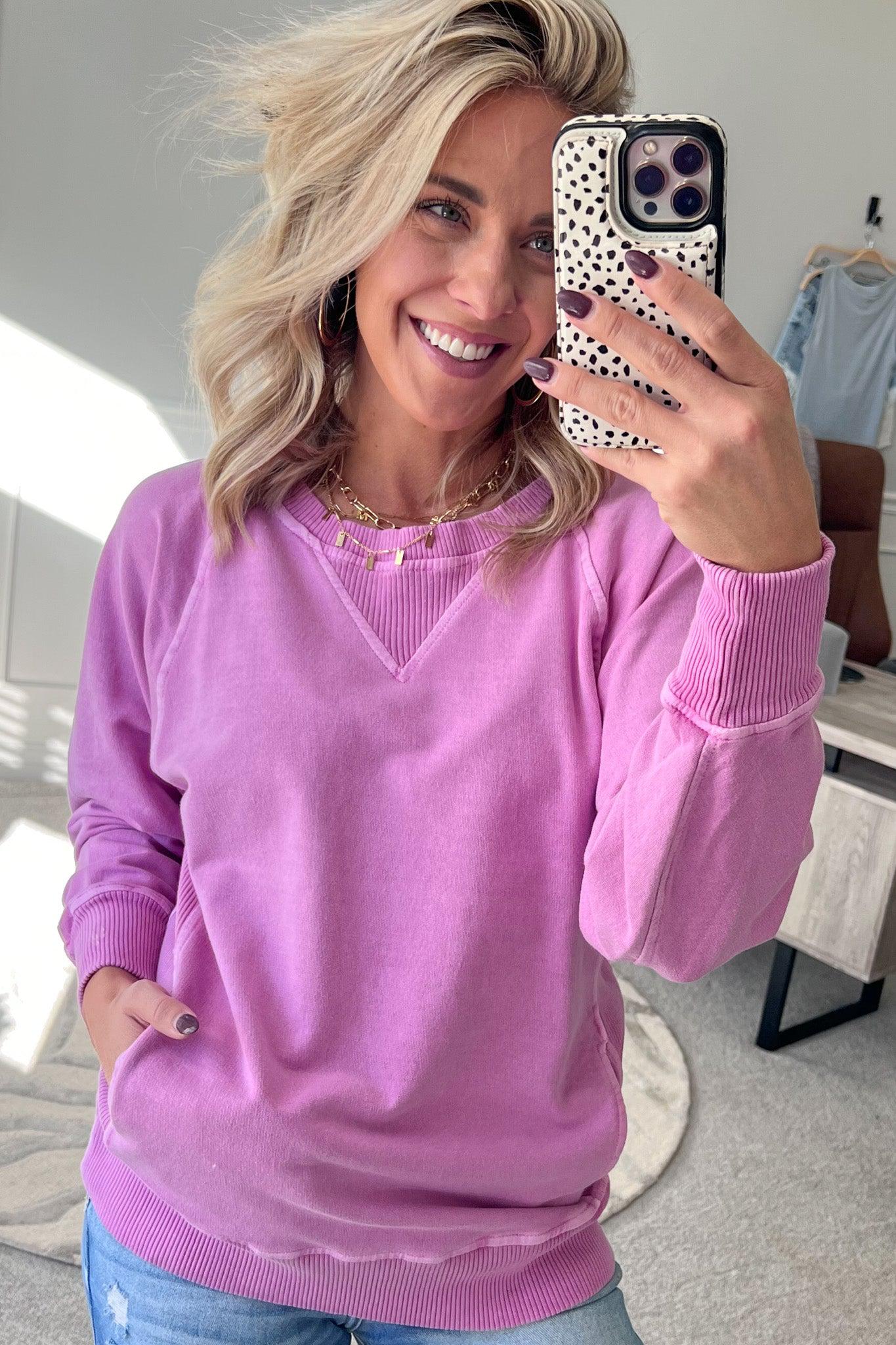 A woman wearing a bright plum ribbed accent pocketed pullover with dolman sleeves and a round neckline.