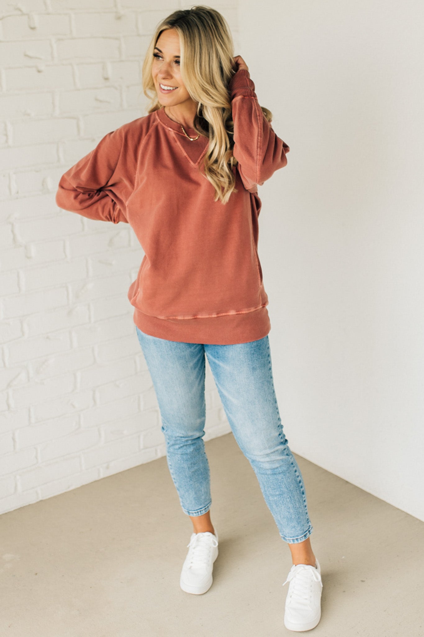 A woman wearing a rust ribbed accent pocketed pullover with dolman sleeves and a round neckline.