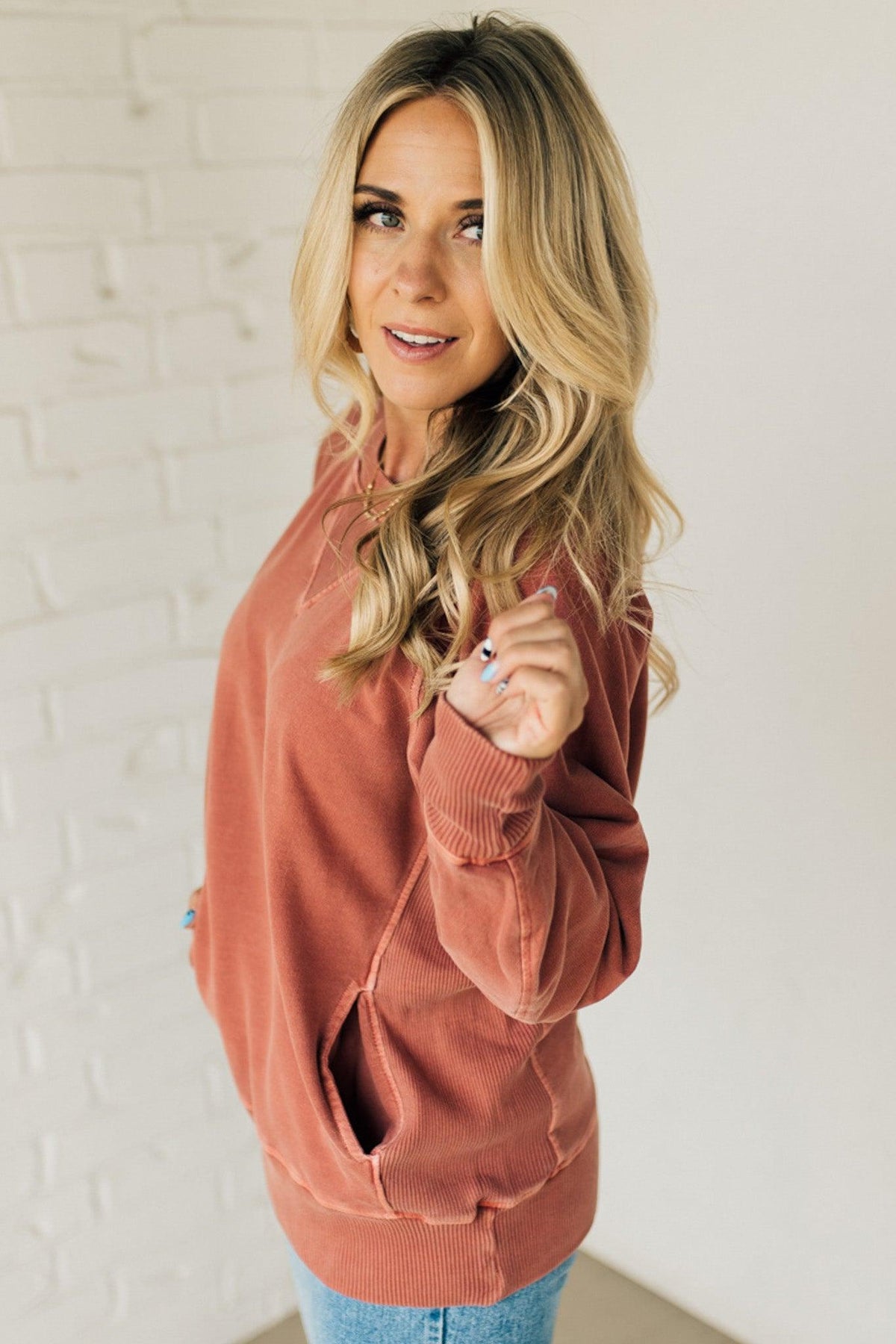 A woman wearing a rust ribbed accent pocketed pullover with dolman sleeves and a round neckline.