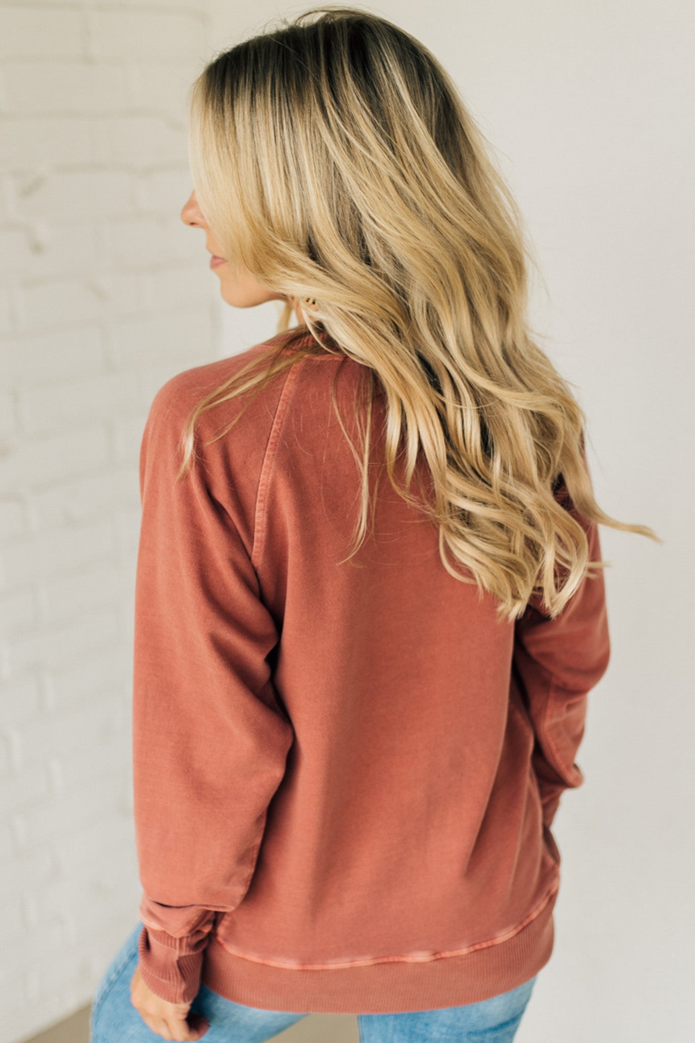 A woman wearing a rust ribbed accent pocketed pullover with dolman sleeves and a round neckline.