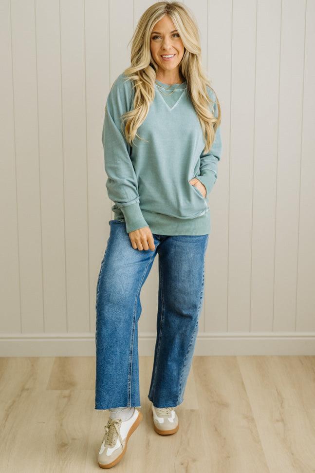 Woman wearing a light blue sweater and jeans standing against a white paneled wall.