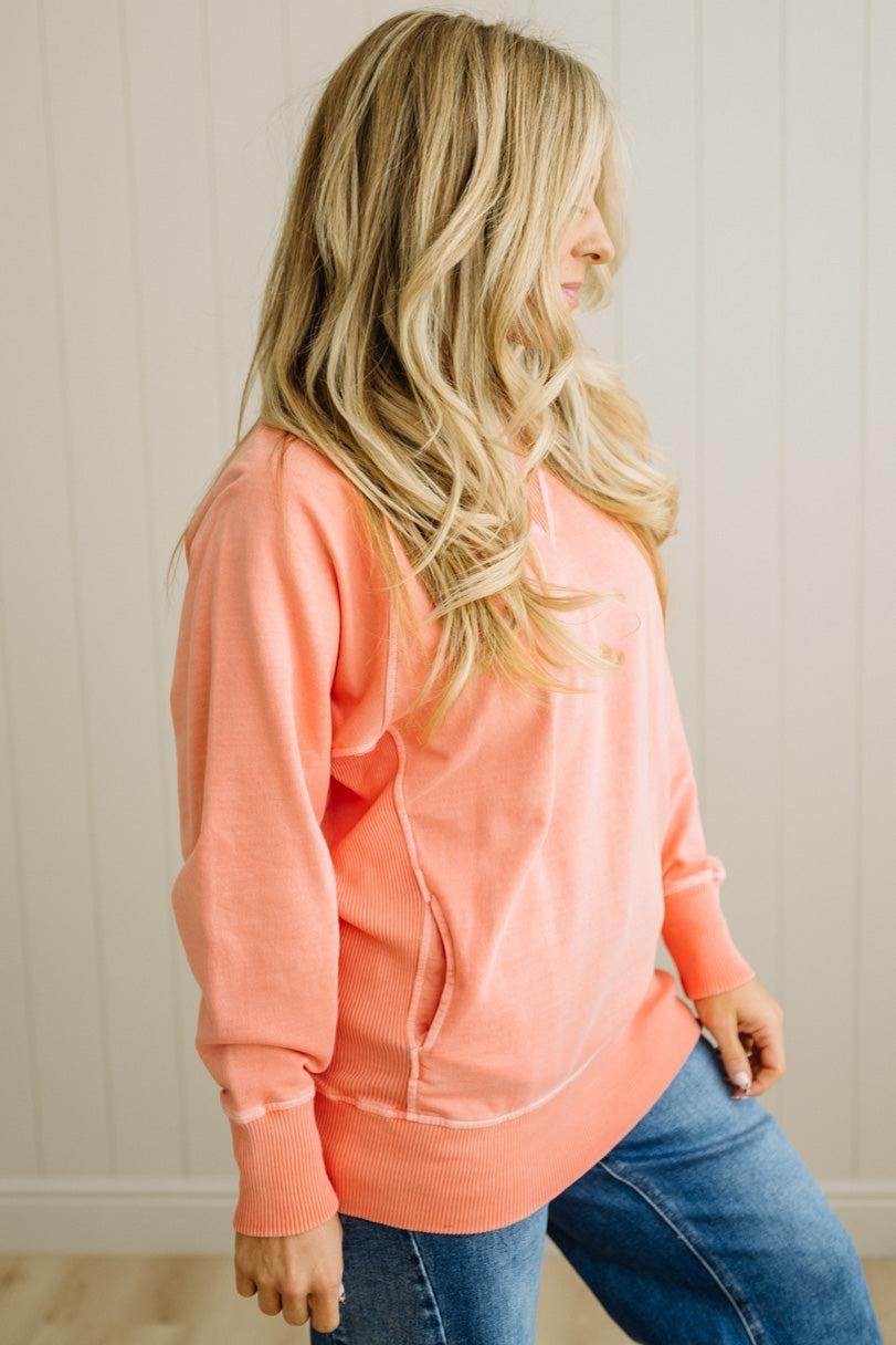 Woman wearing a coral sweatshirt and blue jeans against a neutral background