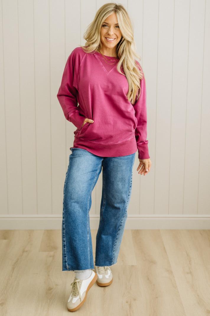 Woman wearing a pink sweater and blue jeans standing against a white paneled wall.