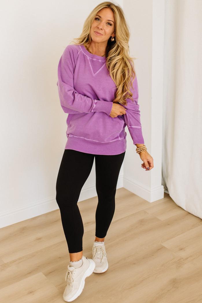 Woman wearing a purple sweatshirt and black leggings indoors.