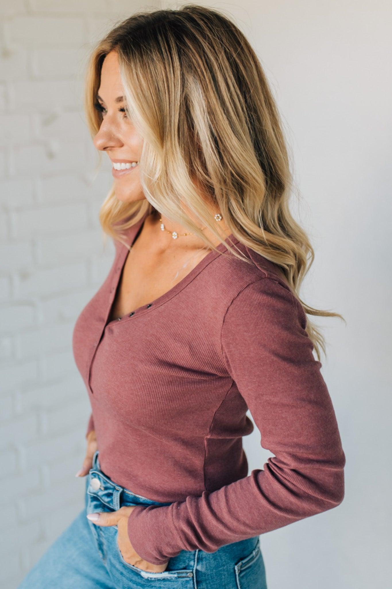 Woman wearing a mauve long-sleeve top and blue jeans against a light gray background