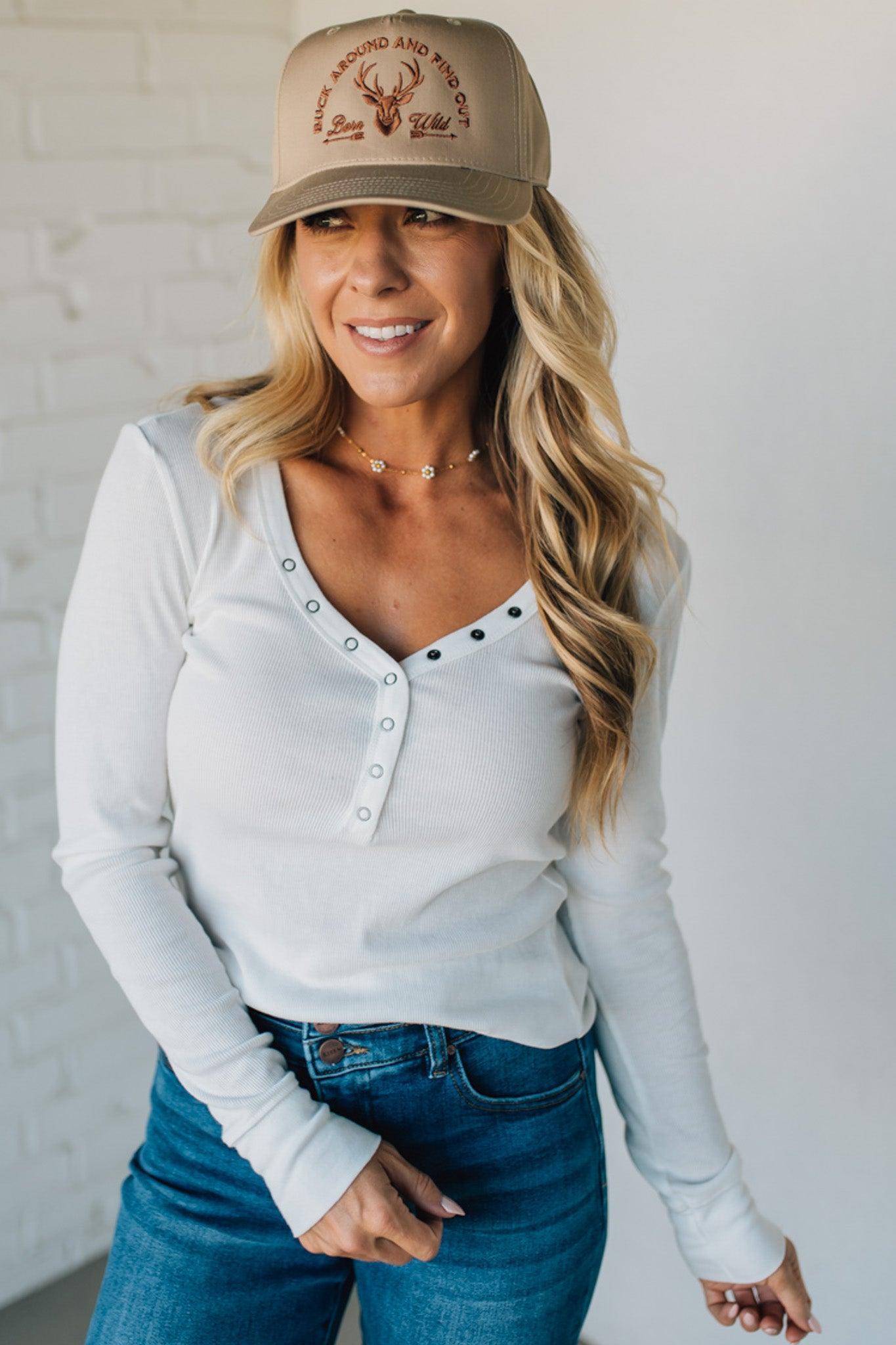 Woman wearing a beige cap with a logo, white long-sleeve shirt, and blue jeans against a white background