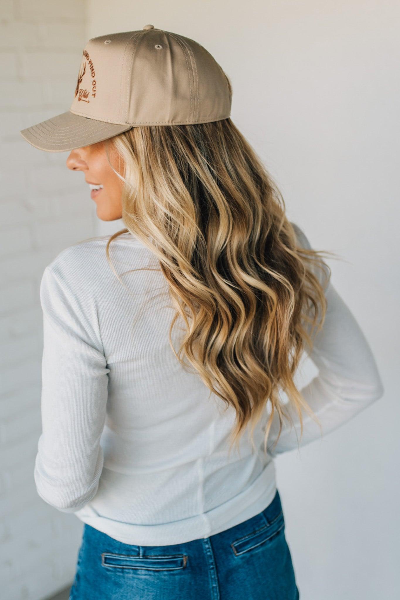 Woman wearing a beige cap and light gray long-sleeve shirt against a plain background