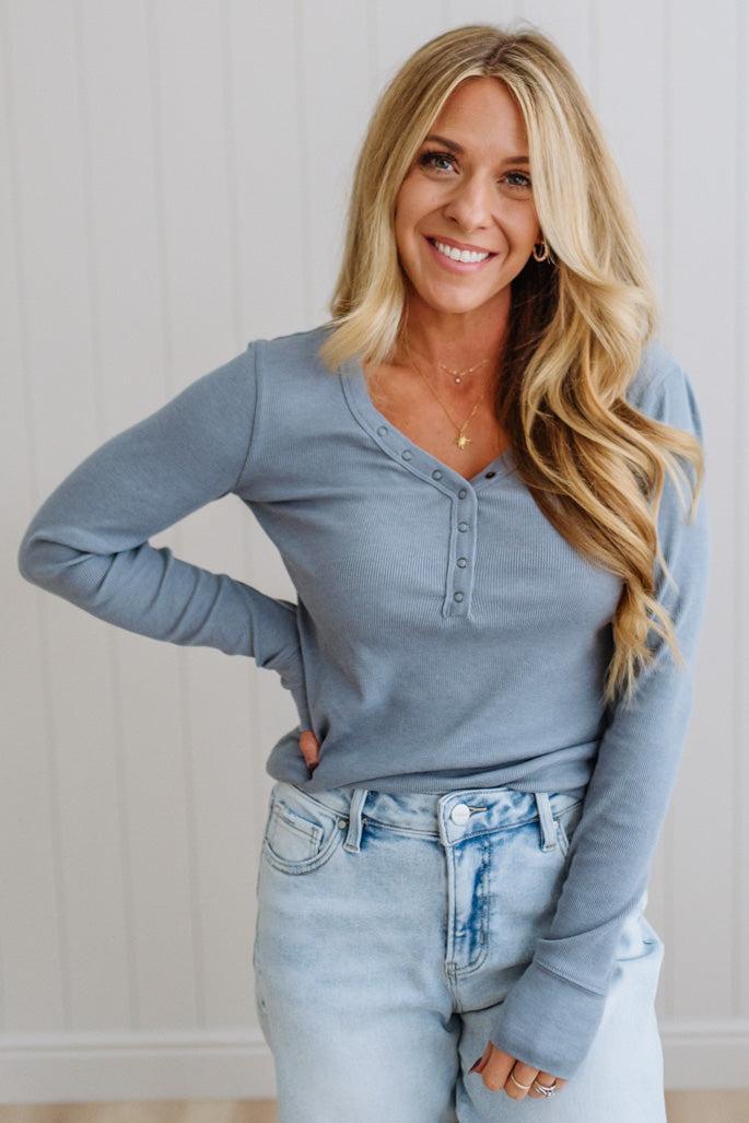 Woman wearing a blue long-sleeve top and light blue jeans against a white wall.