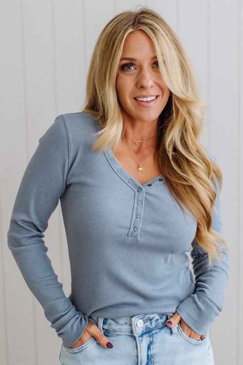 Woman wearing a light blue long-sleeve top and jeans against a white background