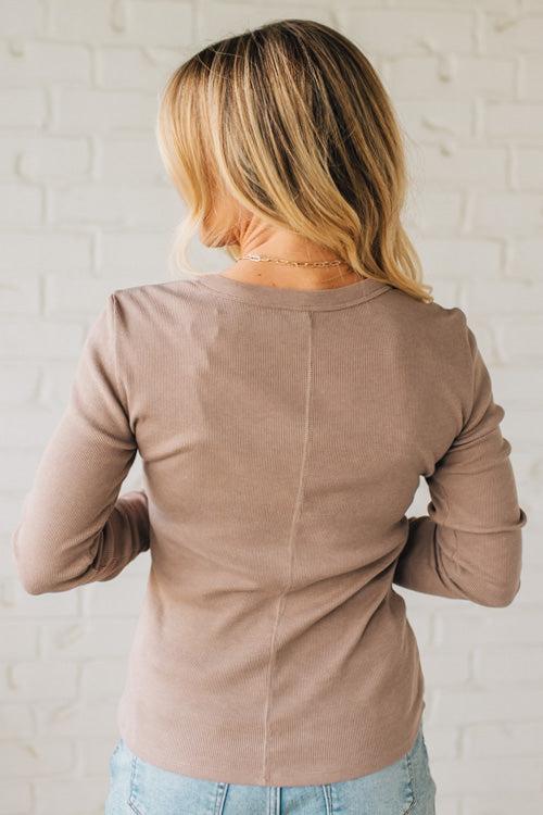 Woman wearing a brown long-sleeve top against a white brick wall.
