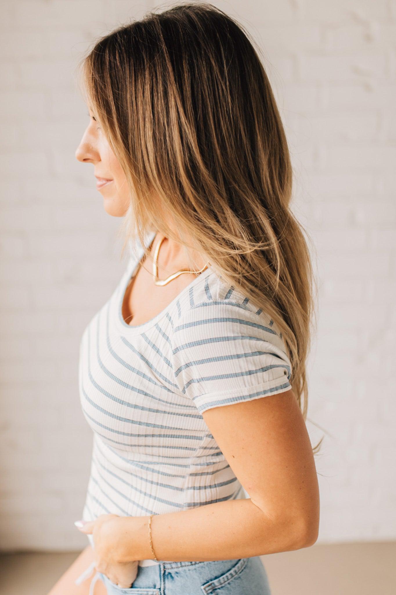 Blonde woman wearing a scoop neck, slim fit tee with vertical ribbed pattern, and horizontal printed stripes.