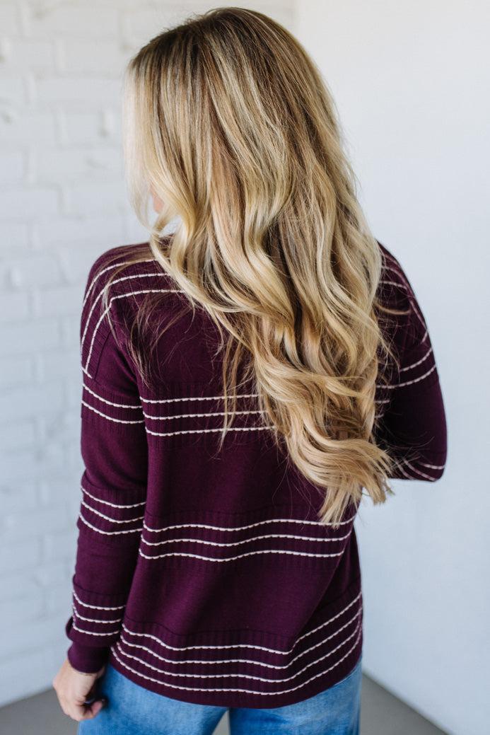 Person wearing a maroon sweater with white stripes, standing against a plain background