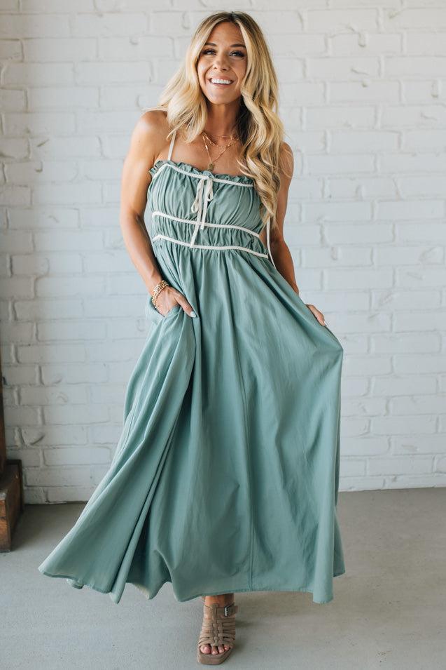 Woman wearing a green strapless dress with white lace details against a white brick wall.