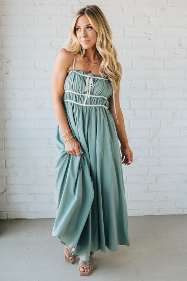 Woman wearing a light green dress with white lace details against a white brick wall.
