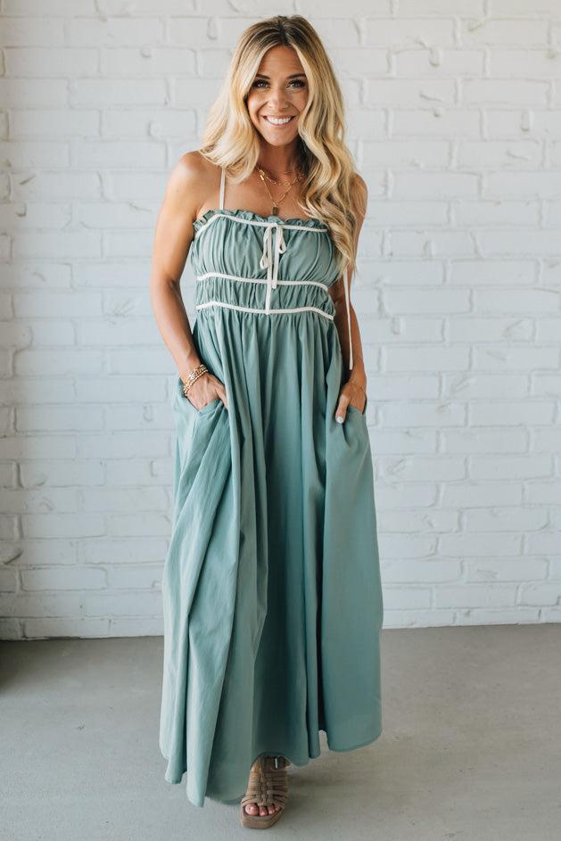 Woman wearing a light blue dress with white buttons against a white brick wall.