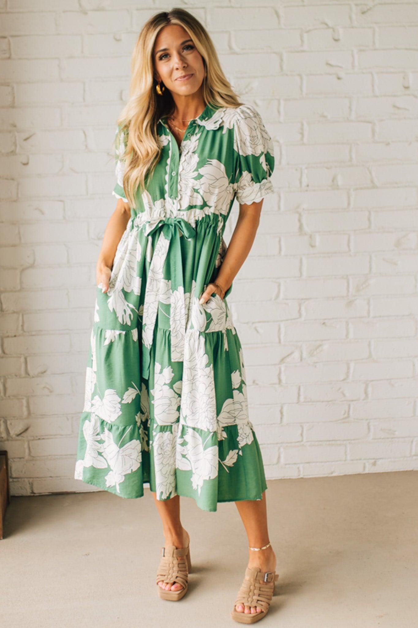 Blonde woman wearing a flower print midi dress with collared neck features buttoned closure, belted waistline, side pockets, puffed short sleeves, tiered layer skirt, and trimming along sleeves and neck.