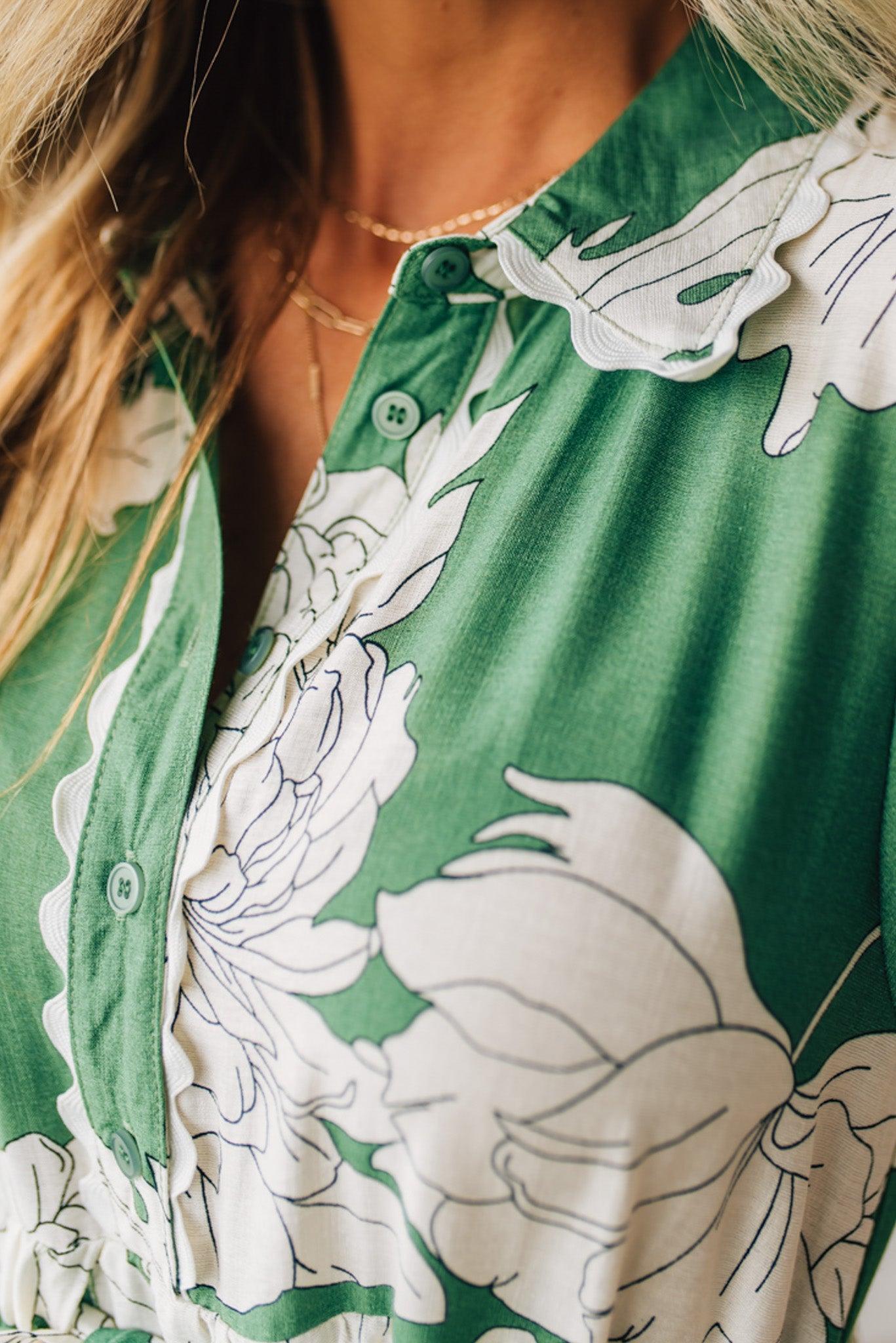Blonde woman wearing a flower print midi dress with collared neck features buttoned closure, belted waistline, side pockets, puffed short sleeves, tiered layer skirt, and trimming along sleeves and neck.
