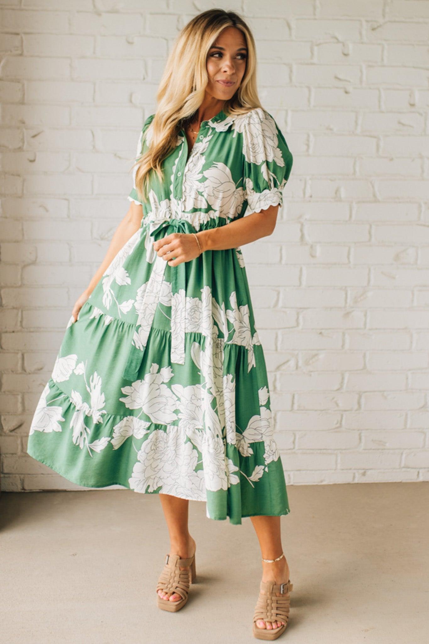 Blonde woman wearing a flower print midi dress with collared neck features buttoned closure, belted waistline, side pockets, puffed short sleeves, tiered layer skirt, and trimming along sleeves and neck.