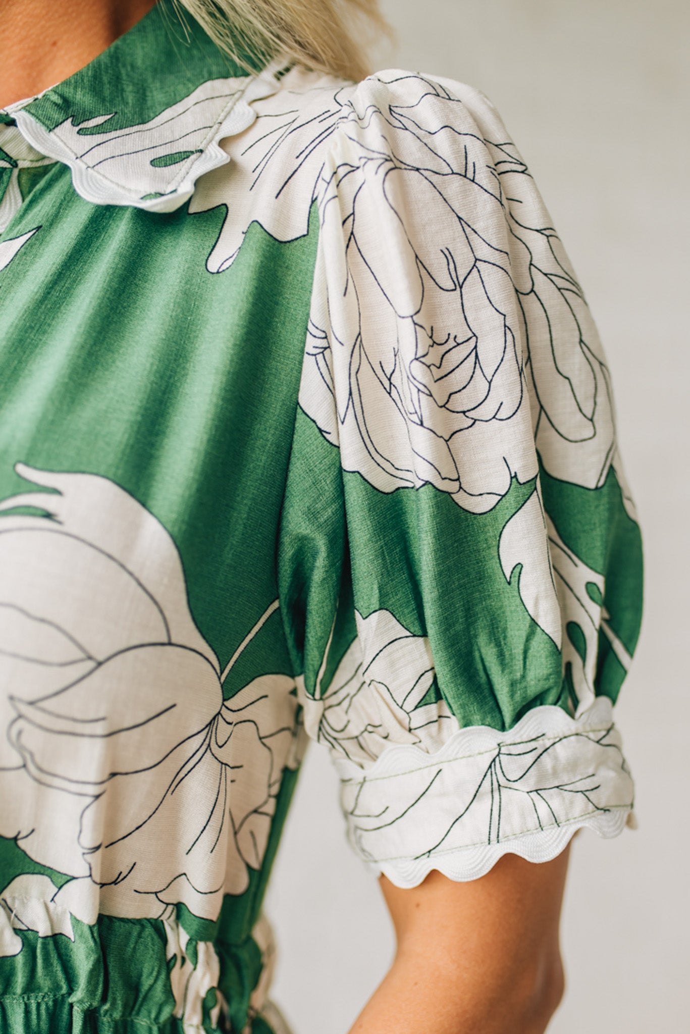 Blonde woman wearing a flower print midi dress with collared neck features buttoned closure, belted waistline, side pockets, puffed short sleeves, tiered layer skirt, and trimming along sleeves and neck.