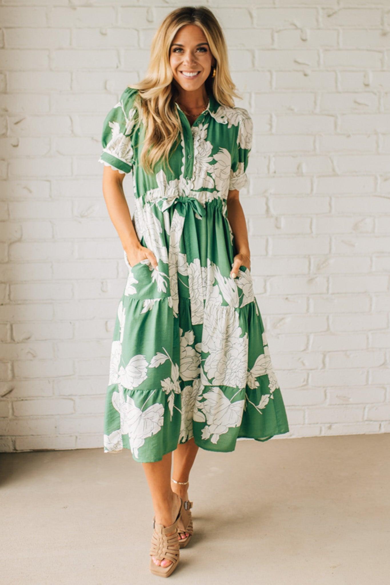 Blonde woman wearing a flower print midi dress with collared neck features buttoned closure, belted waistline, side pockets, puffed short sleeves, tiered layer skirt, and trimming along sleeves and neck.