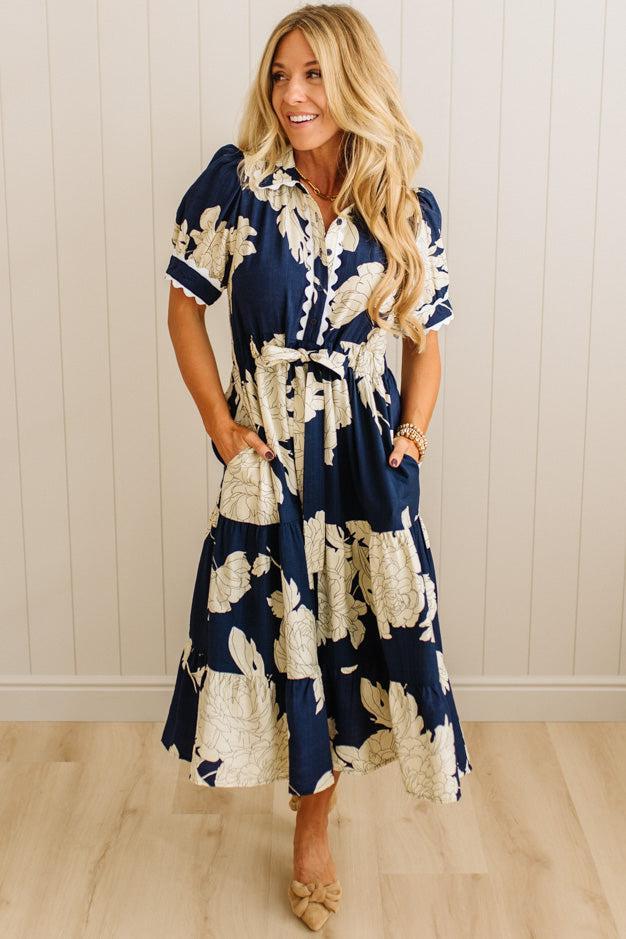 Woman wearing a navy blue floral dress against a white paneled wall.
