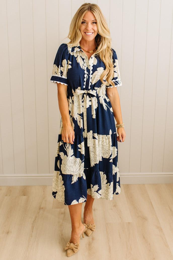 Woman wearing a navy floral dress standing against a white paneled wall.