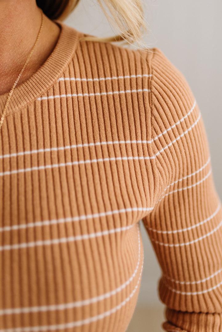 BLONDE WOMAN IN A STUDIO WEARING JEANS AND A BIG BELT WITH A CAMEL RIBBED, LONG SLEEVE, CREW NECK, SUPER STRETCHY BASIC STRIPED INNER SWEATER.