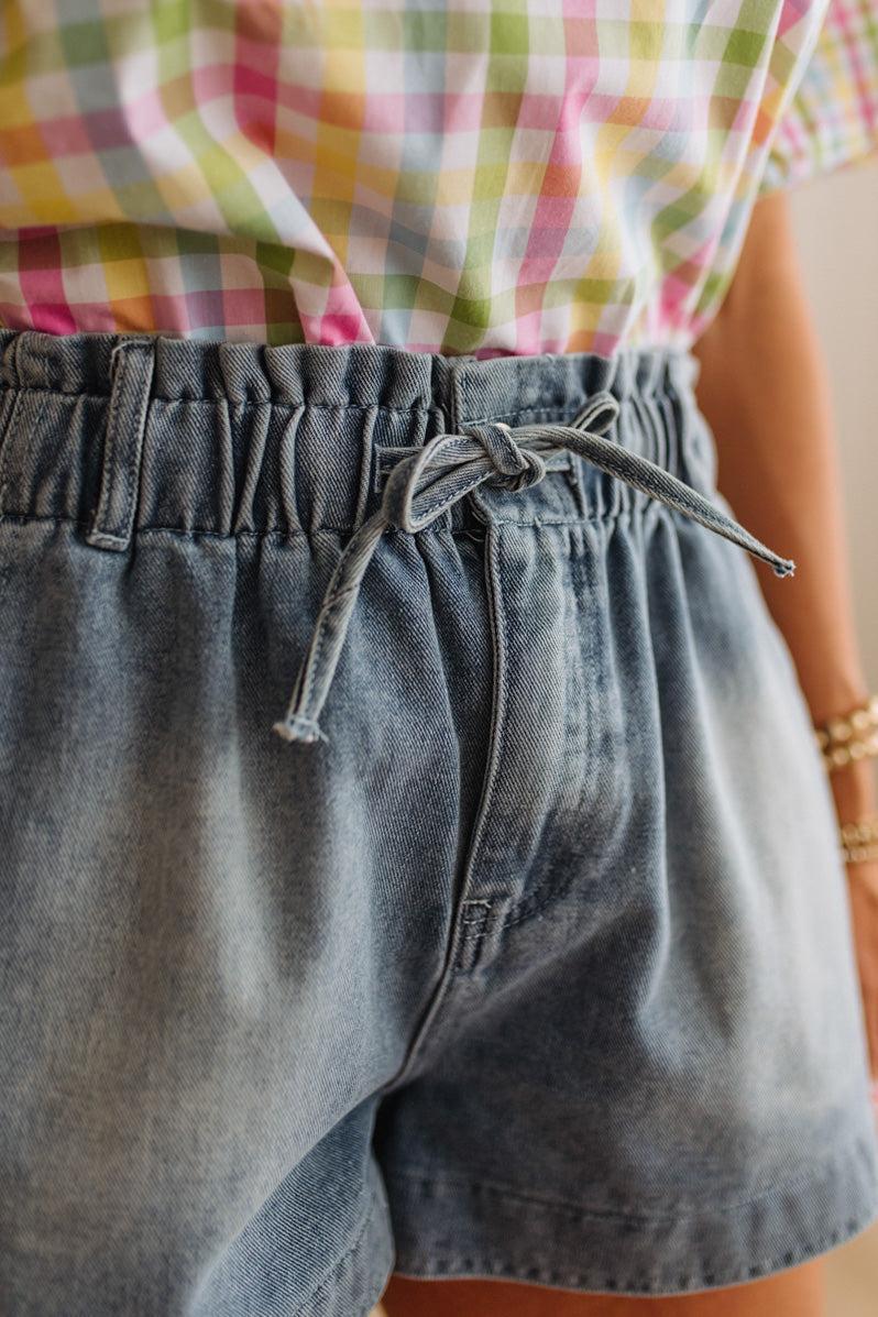 Person wearing a colorful plaid shirt and gray shorts with a blurred background