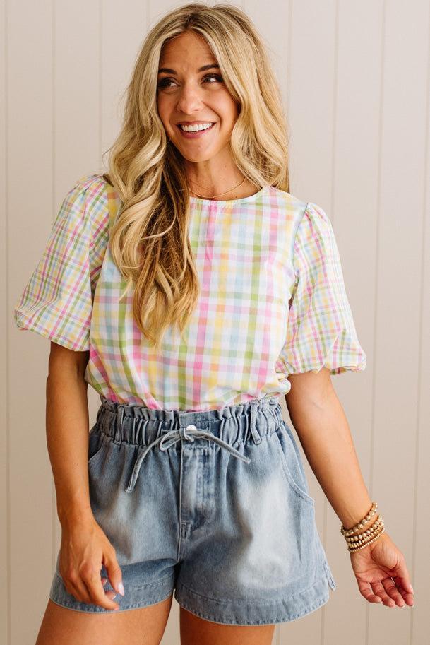 Woman wearing a pastel checkered top and denim shorts against a neutral background