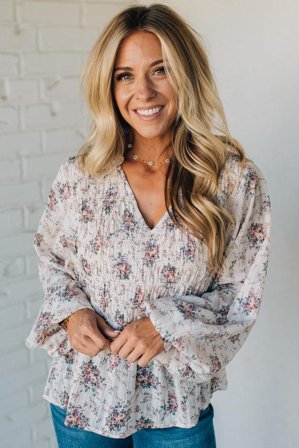 Woman wearing a floral blouse against a white brick wall
