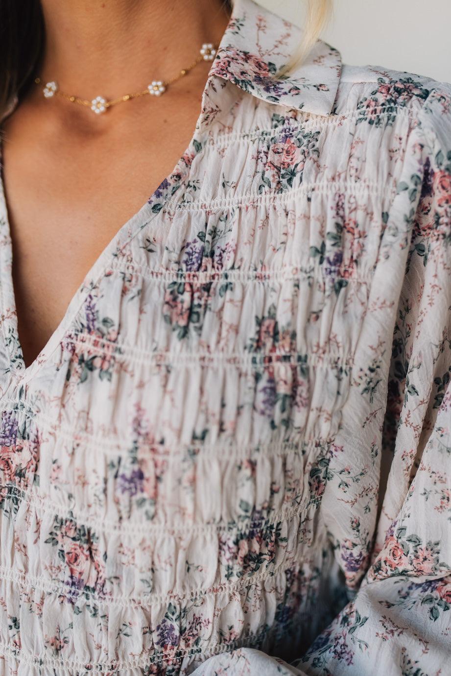 Close-up of a floral top with a necklace worn by a person.