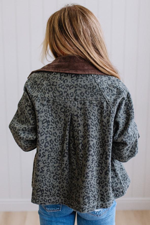 Blonde woman wearing a leopard print barn jacket with brown corduroy collar and gingham plant lining. Standing on a light wood floor with panel backdrop.
