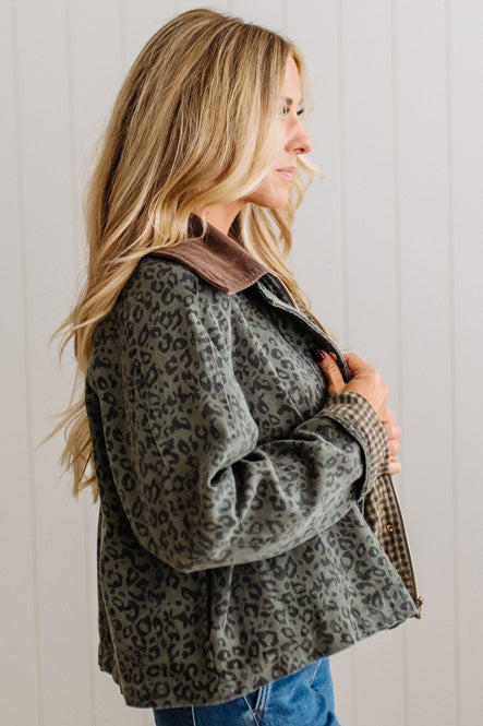 A woman wearing a dark gray and black leopard print jacket with a brown corduroy collar, shown in profile against a white paneled wall.