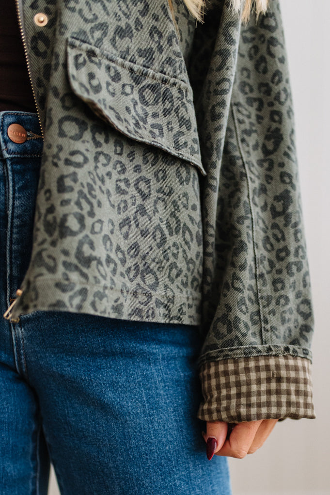 Close-up of a person wearing a leopard-print jacket with a brown and beige gingham cuff, paired with blue jeans.