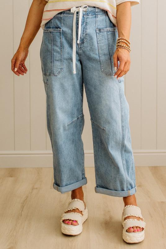 Person wearing blue jeans and white sandals on a light wooden floor.