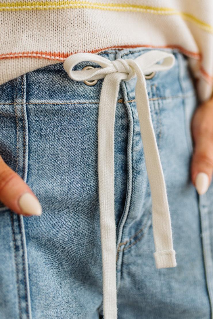 Close-up of a person wearing blue jeans with a drawstring, focusing on the waistband.