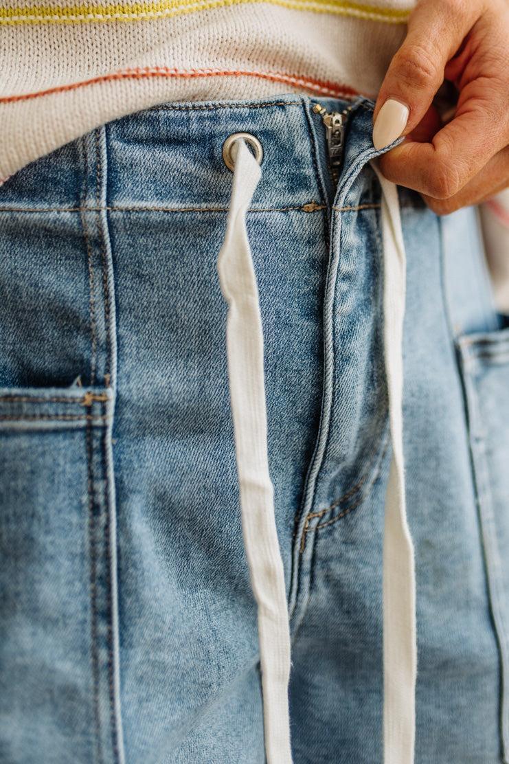 Close-up of a person adjusting the waistband of blue jeans.