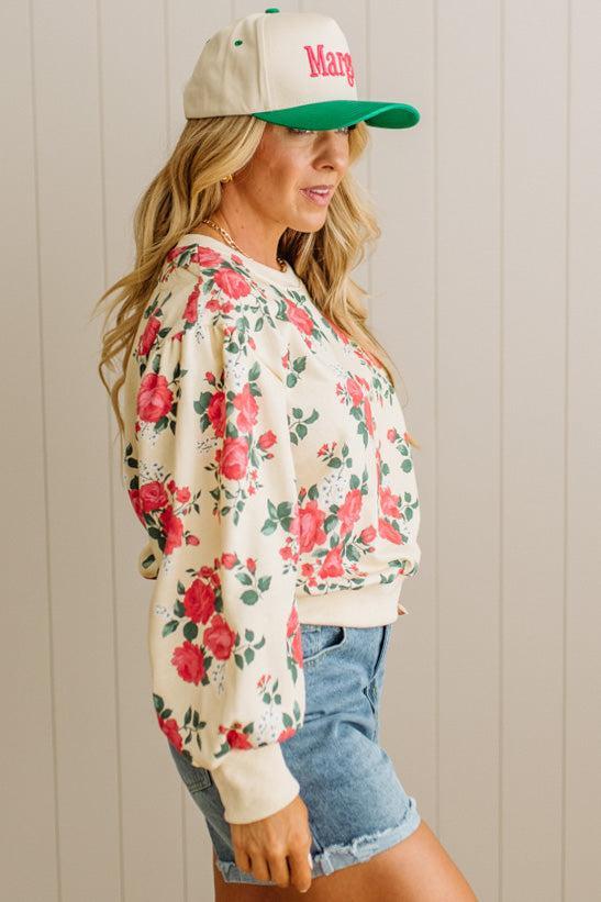 Woman wearing a floral sweatshirt and cap with 'Mary' printed on it against a neutral background