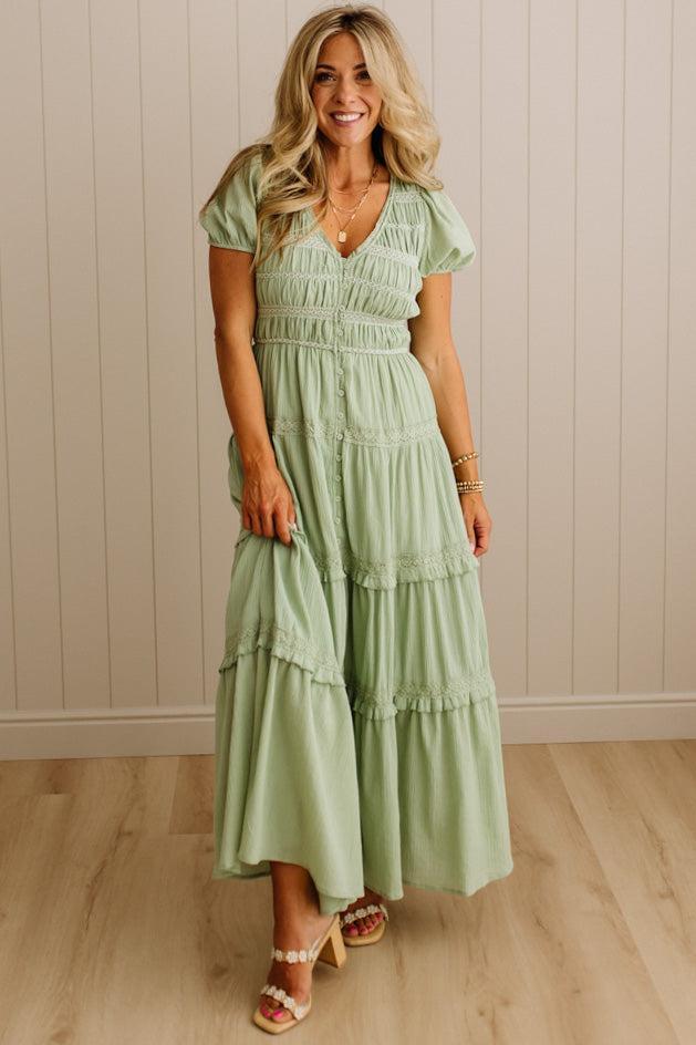 Woman wearing a green dress standing against a beige wall.