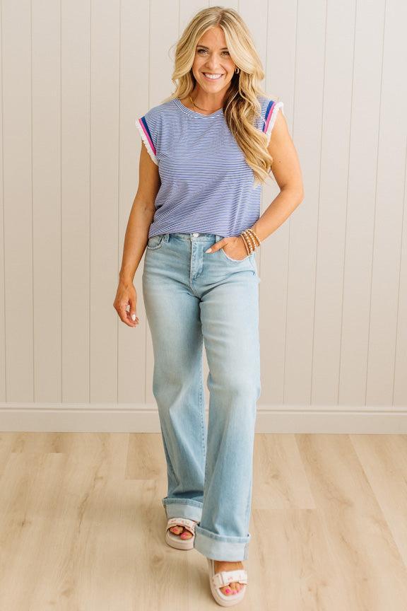 Woman wearing a striped shirt and light blue jeans standing against a plain wall.