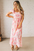 Blonde woman wearing a maxi dress with floral pink and a dark pink print, ruffle sleeved, with back smocked panel.