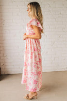 Blonde woman wearing a maxi dress with floral pink and a dark pink print, ruffle sleeved, with back smocked panel.