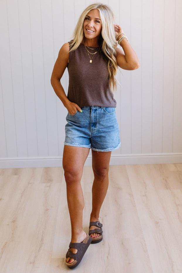 Woman wearing a brown tank top and denim shorts standing on a wooden floor.