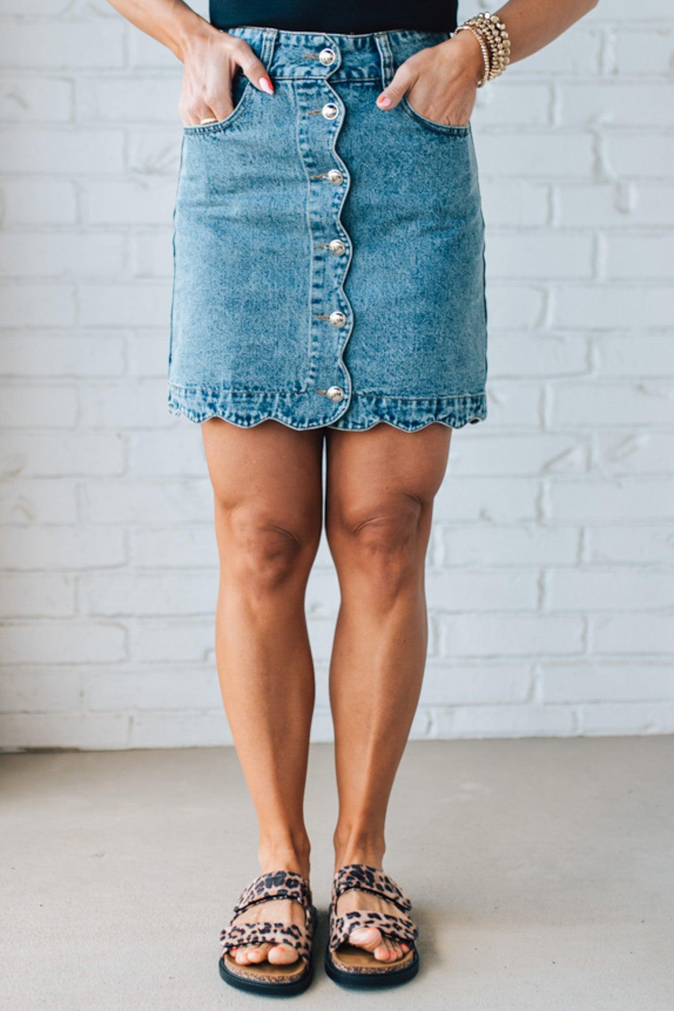 BLONDE WOMAN IN A HAT AND BLACK TANK WEARING A SCALLOP BUTTONED FRONT DENIM SKIRT.