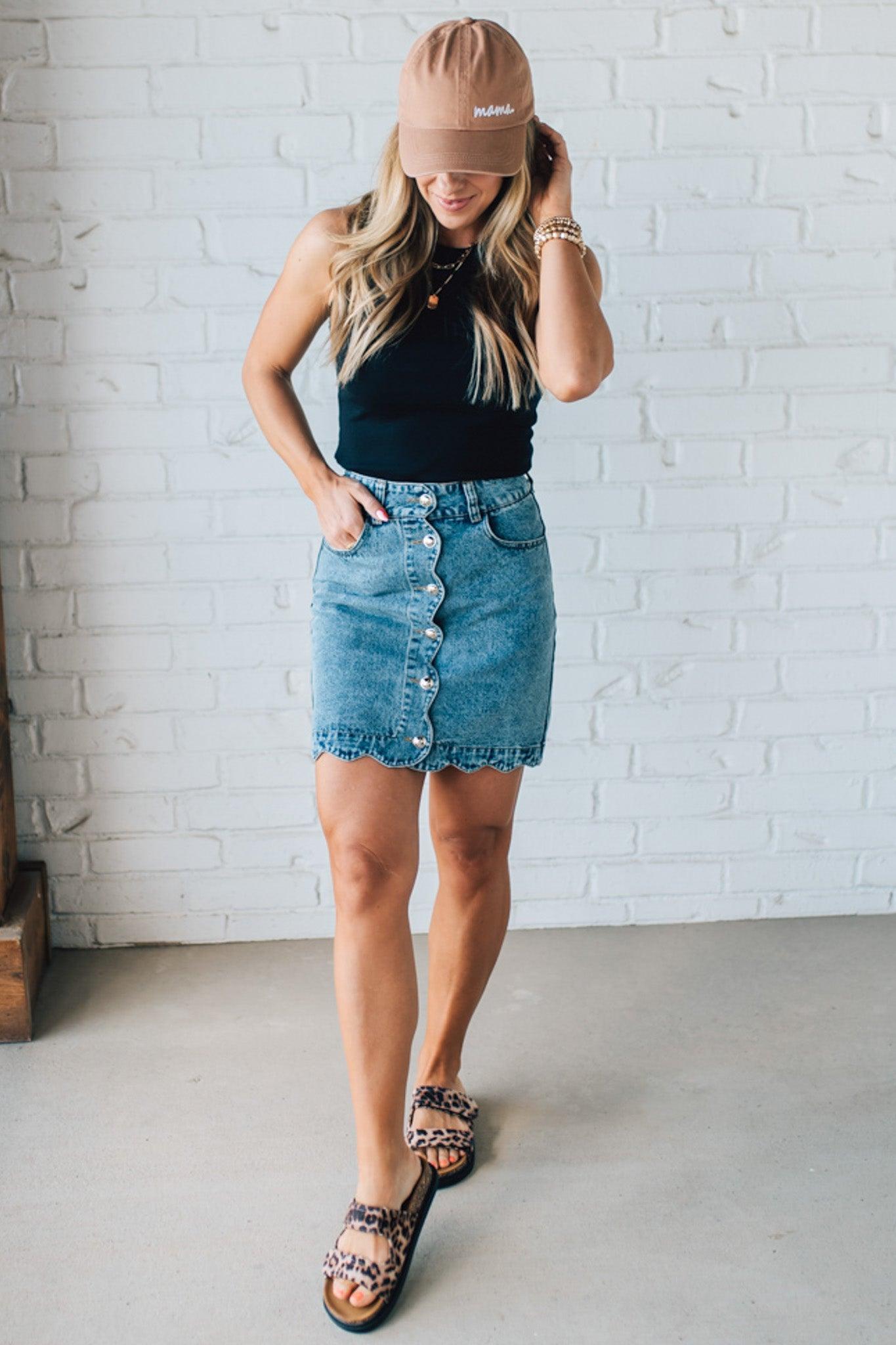 BLONDE WOMAN IN A HAT AND BLACK TANK WEARING A SCALLOP BUTTONED FRONT DENIM SKIRT.