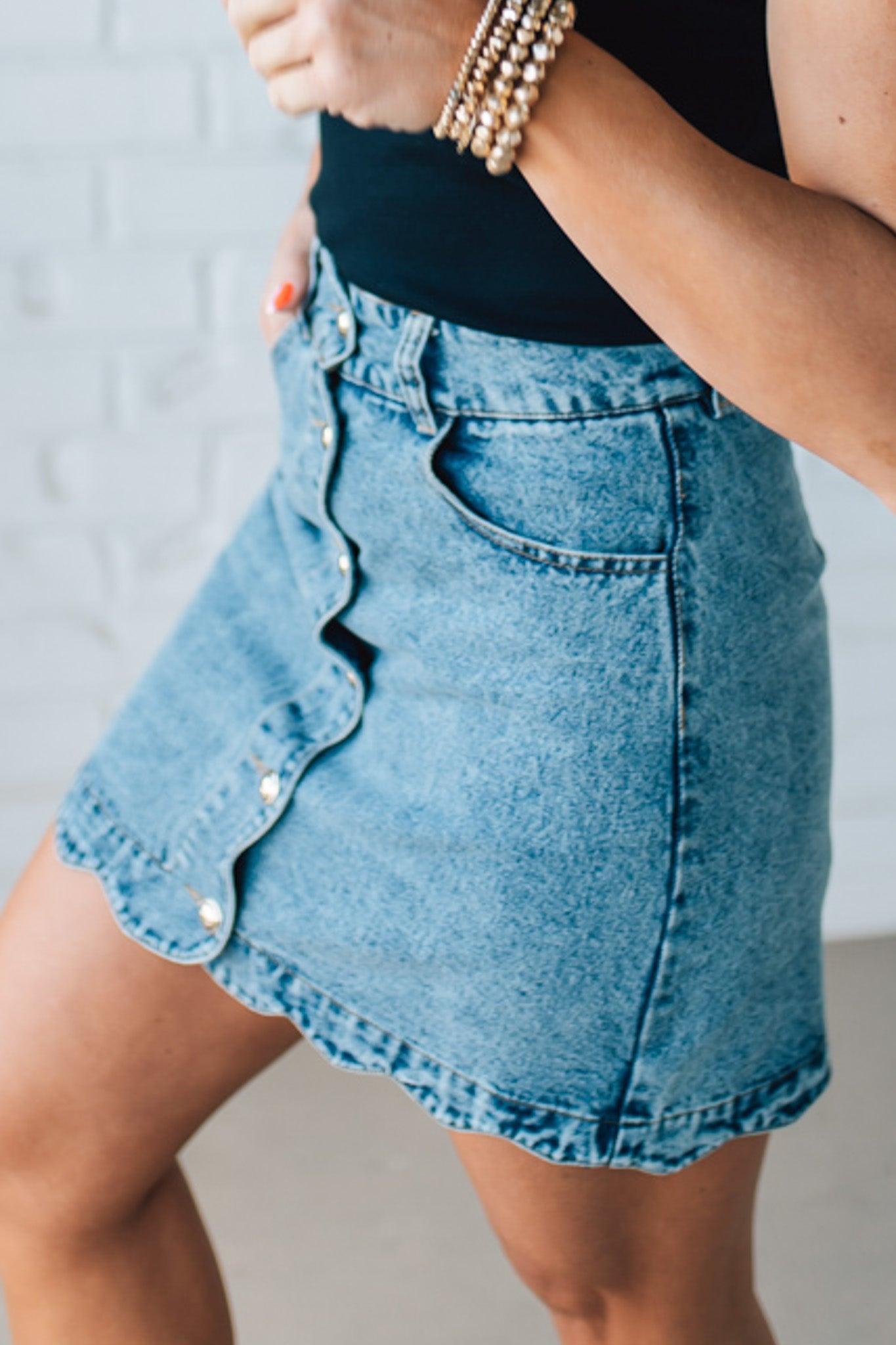 BLONDE WOMAN IN A HAT AND BLACK TANK WEARING A SCALLOP BUTTONED FRONT DENIM SKIRT.