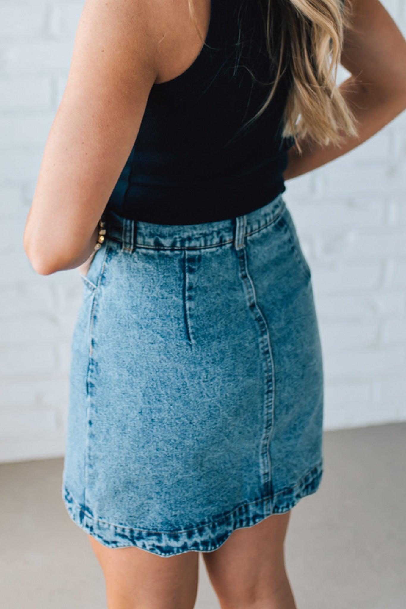 BLONDE WOMAN IN A HAT AND BLACK TANK WEARING A SCALLOP BUTTONED FRONT DENIM SKIRT.