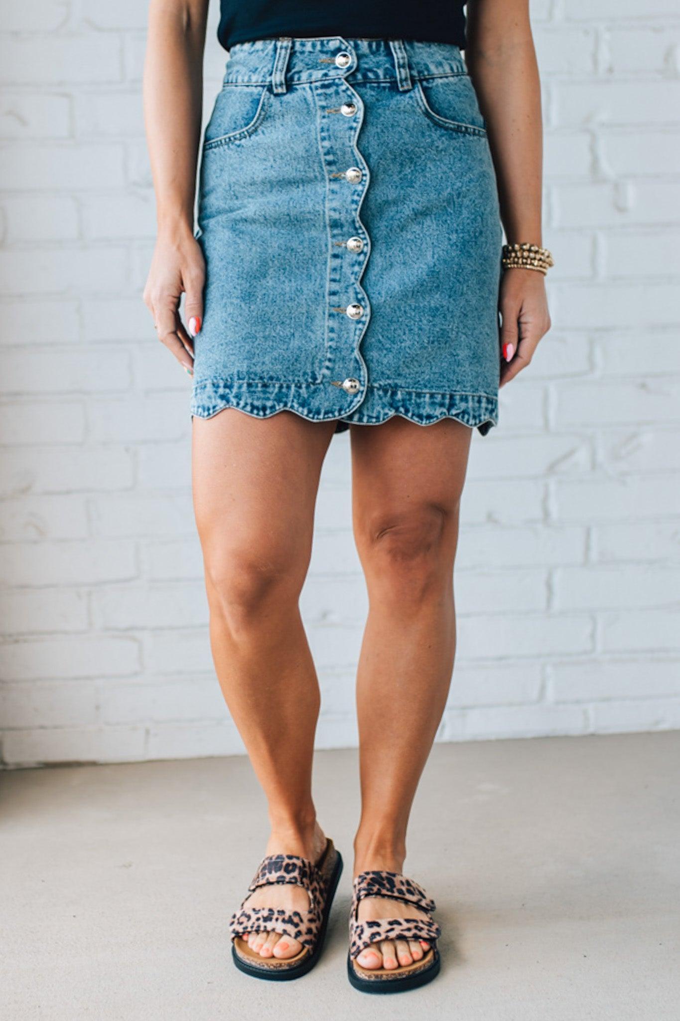 BLONDE WOMAN IN A HAT AND BLACK TANK WEARING A SCALLOP BUTTONED FRONT DENIM SKIRT.