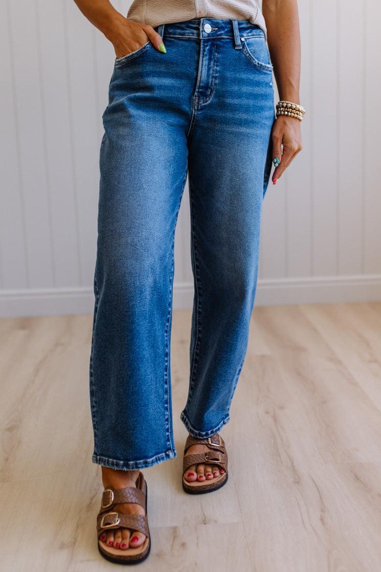 Person wearing blue jeans and sandals indoors with a neutral background